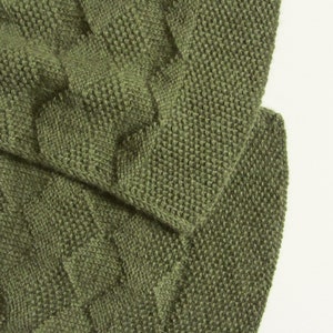 Könnte beinhalten: Nahaufnahme eines grünen Strickstoffes mit einem Zopfmuster.