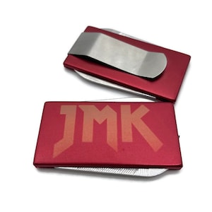 May include: Red metal money clip with a silver clip and the letters "JMK" engraved on the front.