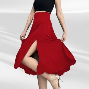 May include: A red skirt with a high waist and a front slit. The skirt is knee-length and has a flowy silhouette. The model is wearing a black crop top and gold heels.