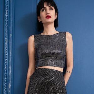 May include: A woman wearing a silver sequined crop top and a black sequined skirt. The skirt is a pencil skirt with a high waist.