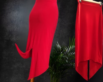 May include: Two red skirts with a high slit on the side. The skirt on the left is being held up by a hand, while the skirt on the right is hanging on a hanger. Both skirts have a long, flowing design.