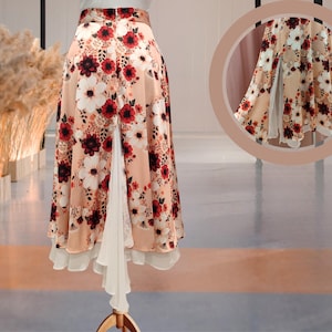 May include: A peach-coloured skirt with a floral print and a white ruffle trim. The skirt has a side slit and a layered design.
