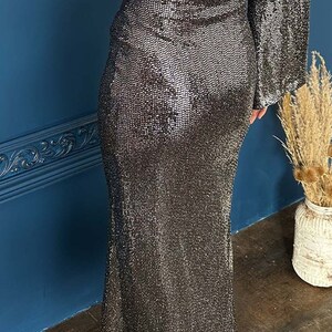 May include: A two-piece silver sequin outfit. The top is a long-sleeved crop top, and the skirt is a floor-length, form-fitting design. The outfit is made of a shimmering, textured fabric, perfect for special occasions.