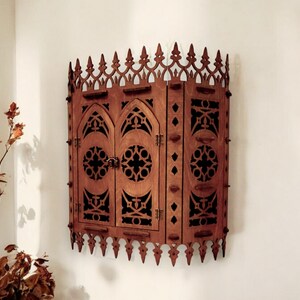 Peut inclure: Une armoire murale en bois de style gothique. L'armoire a deux portes avec des d&eacute;coupes complexes et une forme d'arche pointue. L'armoire est peinte en brun fonc&eacute;.
