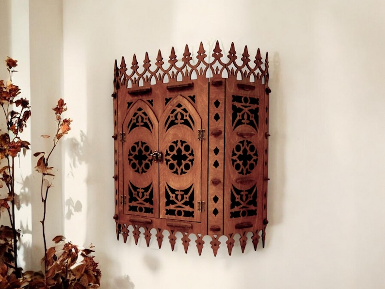 Peut inclure: Une armoire murale en bois de style gothique. L'armoire a deux portes avec des d&eacute;coupes complexes et une forme d'arche pointue. L'armoire est peinte en brun fonc&eacute;.