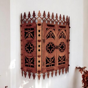 Peut inclure: Une armoire murale en bois de style gothique. L'armoire a deux portes avec des sculptures complexes et une arche en ogive. L'armoire est peinte en brun fonc&eacute;.