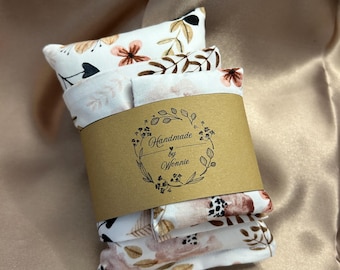 Puede incluir: Un conjunto de tres pequeños artículos de tela rectangulares envueltos con una banda de papel marrón. La tela tiene un fondo blanco con un estampado floral en tonos rosa, marrón y negro. La banda dice "Handmade by Wonnie."