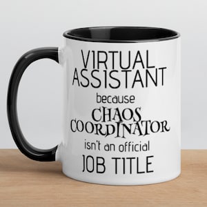 Op de afbeelding: Een witte koffiemok met een zwarte rand en handvat. De mok heeft zwarte tekst die luidt "Virtuele assistent omdat Chaoscoördinator geen officiële functietitel is."