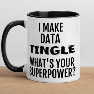 Op de afbeelding: Een witte keramische mok met een zwarte rand en handvat. De mok heeft zwarte tekst met de tekst "I make data tingle. What's your superpower?"