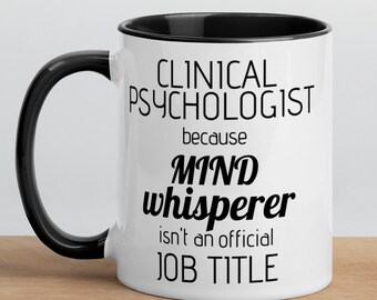 May include: White ceramic mug with a black rim and handle. The mug has black text that reads "Clinical Psychologist because Mind Whisperer isn't an official Job Title."