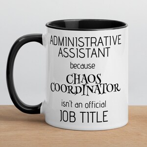 May include: White ceramic mug with a black handle and black rim. The mug has black text that reads "Administrative Assistant because Chaos Coordinator isn't an official job title."