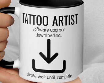 Könnte beinhalten: Eine weiße Kaffeetasse mit schwarzem Rand und Henkel. Die Tasse hat einen schwarzen Text, der "Tattoo Artist software upgrade downloading..." mit einem schwarzen Abwärtspfeil-Symbol und dem Text "please wait until complete" lautet.