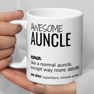 Può includere: Una tazza in ceramica bianca con un designo nero che recita "AWESOME AUNCLE" e definisce la parola come "come uno zio normale, tranne che molto più fantastico." La tazza dice anche "vedi anche: supereroe, operatore di miracoli."