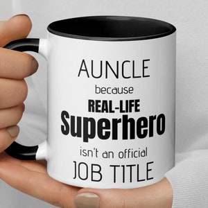 Può includere: Una tazza da caffè bianca con bordo e manico neri. La tazza ha un testo nero che recita "AUNCLE because REAL-LIFE SUPERHERO isn't an official JOB TITLE".