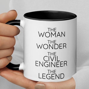 Op de afbeelding: Een witte keramische mok met een zwarte rand en handvat. De mok heeft zwarte tekst met de tekst "The Woman The Wonder The Civil Engineer The Legend".