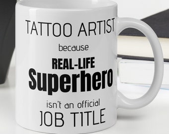 Könnte beinhalten: Weiße Keramiktasse mit schwarzem Text, der "Tattoo Artist because Real-Life Superhero isn't an official Job Title" lautet