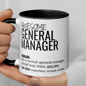 Può includere: Una tazza da caffè bianca con un bordo e un manico neri. La tazza ha un testo nero che recita "AWESOME GENERAL MANAGER noun like a normal general manager, except way more awesome see also: superhero, miracle worker"