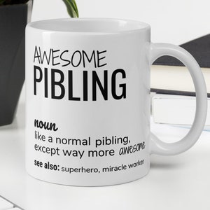 Può includere: Una tazza in ceramica bianca con un designo nero che recita "AWESOME PIBLING" e definisce la parola come "come un pibling normale, tranne che molto più fantastico." La definizione include anche "vedi anche: supereroe, operatore di miracoli."
