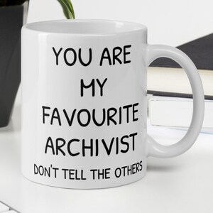 May include: White ceramic mug with black text that reads "You are my favourite archivist. Don't tell the others."