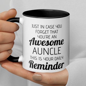 Può includere: Una tazza da caffè in ceramica bianca con bordo e manico neri. La tazza ha un testo nero che recita "Just in case you forget that you're an Awesome Auncle. This is your daily reminder."