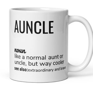 Può includere: Una tazza in ceramica bianca con una grafica nera che recita "AUNCLE" e definisce la parola come "come una zia o uno zio normale, ma molto più cool." La definizione include anche "vedi anche: straordinario e coraggioso."