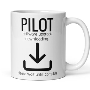 Peut inclure: Une tasse à café en céramique blanche avec du texte noir qui dit "PILOT software upgrade downloading..." avec une flèche noire vers le bas et un rectangle noir sous la flèche. Le texte sous la flèche dit "please wait until complete."