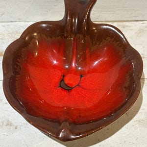 May include: A ceramic leaf-shaped bowl with a glossy finish. The interior is a vibrant red, transitioning to a dark brown rim and handle. The bowl's design features a central black accent.