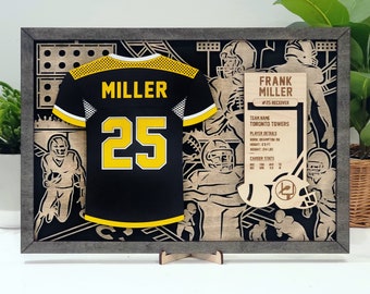 May include: A wooden framed shadow box with a black and yellow football jersey with the name "MILLER" and the number "25" on the back. The box also includes a wooden plaque with the player's name, team name, and stats.