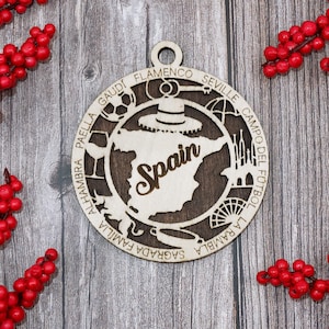 May include: Wooden Spain ornament with a cutout design. The ornament features the word "Spain" in the center, surrounded by iconic Spanish elements and landmarks. The ornament is circular with a hole at the top for hanging.