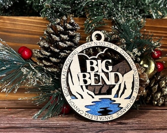 Puede incluir: Un adorno de madera con forma de círculo con un diseño azul y marrón del Parque Nacional Big Bend en Texas. El adorno tiene el texto "Big Bend" en letras blancas grandes y las coordenadas "29.25° N 103.25° W" y el texto "Boquillas Crossing Santa Elena Canyon" y "Chihuahuan Desert Rio Grande" alrededor del borde.
