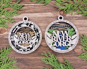 Könnte beinhalten: Zwei Holzornamente mit einem Laser-geschnittenen Design der New River Gorge Bridge in West Virginia. Der Text "New River Gorge" ist auf beiden Ornamenten zu sehen. Ein Ornament hat eine goldfarbene Brücke und das andere eine blaue Brücke.