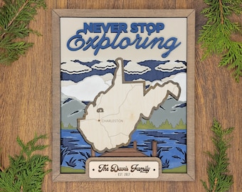 May include: A framed wooden wall art piece with a layered design. The artwork features the text "NEVER STOP Exploring" above a map of West Virginia, with "Charleston" marked. The bottom has a plaque that reads "The Davis Family EST. 2017".