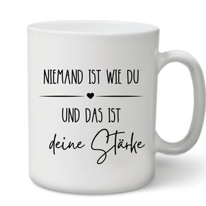 K&ouml;nnte beinhalten: Wei&szlig;e Keramiktasse mit schwarzem Text, der "Niemand ist wie du und das ist deine St&auml;rke" lautet, mit einem kleinen schwarzen Herzen &uuml;ber der zweiten Textzeile.