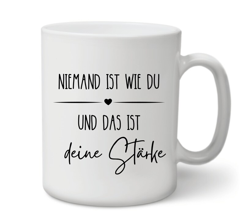 K&ouml;nnte beinhalten: Wei&szlig;e Keramiktasse mit schwarzem Text, der "Niemand ist wie du und das ist deine St&auml;rke" lautet, mit einem kleinen schwarzen Herzen &uuml;ber der zweiten Textzeile.