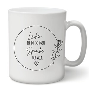 May include: White ceramic mug with a black circle design that says "Lachen ist die sch&ouml;nste Sprache der Welt." with a small heart at the bottom. The circle is surrounded by a black floral design.