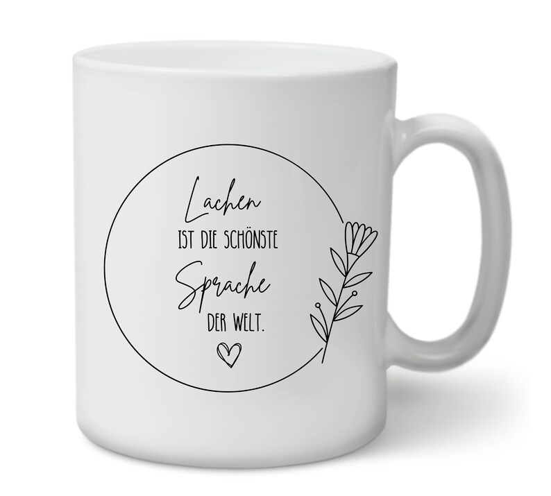 May include: White ceramic mug with a black circle design that says "Lachen ist die sch&ouml;nste Sprache der Welt." with a small heart at the bottom. The circle is surrounded by a black floral design.