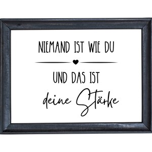 K&ouml;nnte beinhalten: Ein schwarzer gerahmter Druck mit wei&szlig;em Hintergrund und schwarzem Text, der "Niemand ist wie du und das ist deine St&auml;rke" lautet.