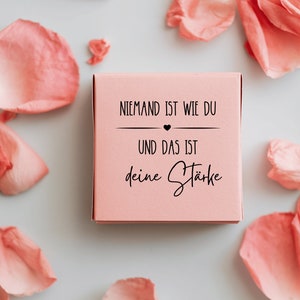 K&ouml;nnte beinhalten: Eine rosa Box mit dem Text "Niemand ist wie du und das ist deine St&auml;rke" (Niemand ist wie du und das ist deine St&auml;rke) in schwarzer Schrift.