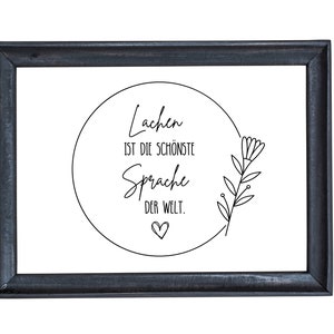 May include: Black framed print with a white background and a circle containing the text "Lachen ist die sch&ouml;nste Sprache der Welt." with a small heart below the text. A simple line drawing of a flower is to the right of the circle.
