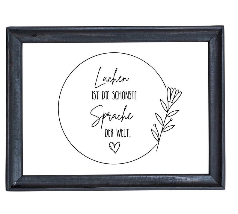 May include: Black framed print with a white background and a circle containing the text "Lachen ist die sch&ouml;nste Sprache der Welt." with a small heart below the text. A simple line drawing of a flower is to the right of the circle.