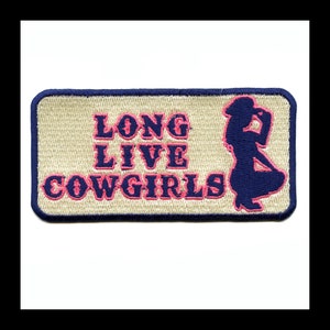 Può includere: Una toppa ricamata beige con un bordo blu scuro. La toppa presenta una silhouette rosa di una cowgirl con il testo "Long Live Cowgirls" in rosa.