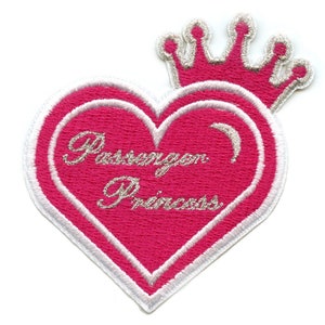 Pode incluir: Patch em forma de coração rosa com contorno branco e uma coroa prateada no topo. O coração tem as palavras "Passion of a Princess" escritas em letras prateadas.
