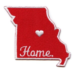 Puede incluir: Parche rojo bordado en forma del estado de Misuri con un corazón blanco en el centro y la palabra "Home" bordada en blanco debajo del corazón.