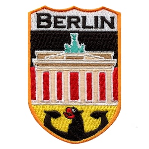 Könnte beinhalten: Ein gestickter Aufnäher mit dem Wort "BERLIN" in weißen Buchstaben auf schwarzem Hintergrund. Der Aufnäher zeigt ein stilisiertes Bild des Brandenburger Tors in Rot, Weiß und Schwarz, mit einem gelben und schwarzen Bären unten.
