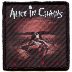 May include: A black and brown woven patch with the band name "Alice in Chains" in white text and the album title "Dirt" in red text. The image shows a woman lying in a red-toned landscape.