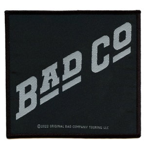 Puede incluir: Un parche cuadrado negro con el texto "BAD CO" en blanco, inclinado diagonalmente a través del parche. El texto está en negrita, sin serif. El texto "©2022 ORIGINAL BAD COMPANY TOURING LLC" está en blanco más pequeño en la parte inferior del parche.
