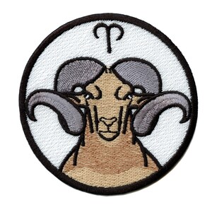 May include: Embroidered patch featuring the astrological symbol for Aries, a ram with large horns. The patch is circular and has a white background with black stitching.