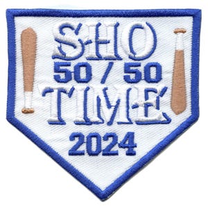 Può includere: Un cerotto bianco e blu a forma di diamante da baseball con il testo "SHO 50/50 TIME 2024" e due mazze da baseball marroni su entrambi i lati.