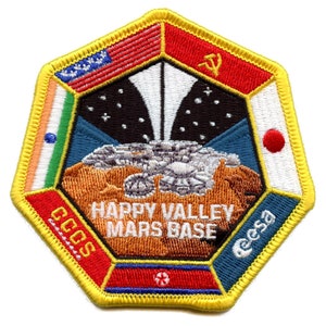 以下が含まれることがあります： 黄色い縁取りの刺繍パッチで、火星基地のデザインが特徴です。パッチには、米国、インド、日本、ソ連の国旗が含まれています。「HAPPY VALLEY MARS BASE」と「CCGS」と「eesa」の文字があります。