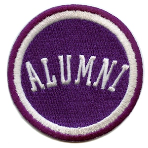 May include: A circular purple patch with the word "ALUMNI" embroidered in white. The patch has a white border and a purple outer edge. The design is simple and classic, suitable for various applications.